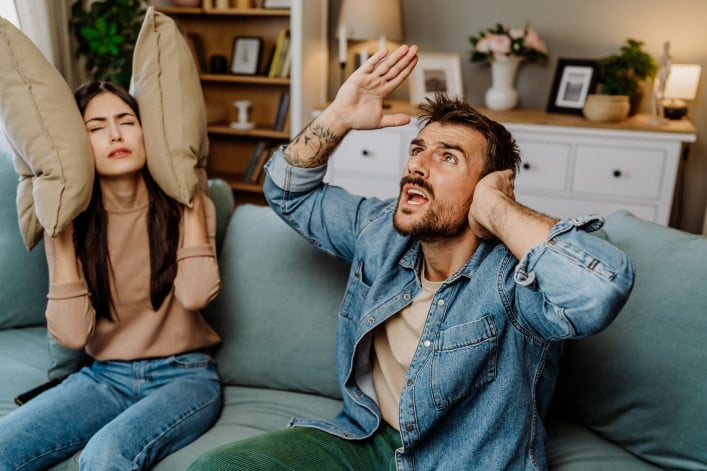 Couple sitting on couch upset by loud neighbors Couple sitting on couch upset by loud neighbors