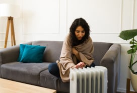 young woman using space heater to supplement apartment heat young woman using space heater to supplement apartment heat
