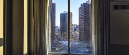 Several skyscraper city apartment buildings viewed through a generic upper east side Manhattan, New York City hotel bedroom window just after dawn sunrise.