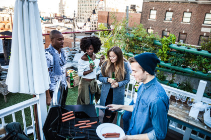 Friends having fun, grilling BBQ and drinking beers together during a rooftop party in New York East Village.