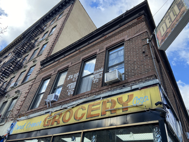 New York, NY USA - December 6, 2023 : Hand-painted yellow and red "Sweet Corner Grocery Corp." sign over a deli on a two-story brick apartment building in Harlem, New York City