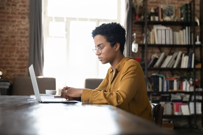 Serious busy young Black laptop user woman working at computer at home office.