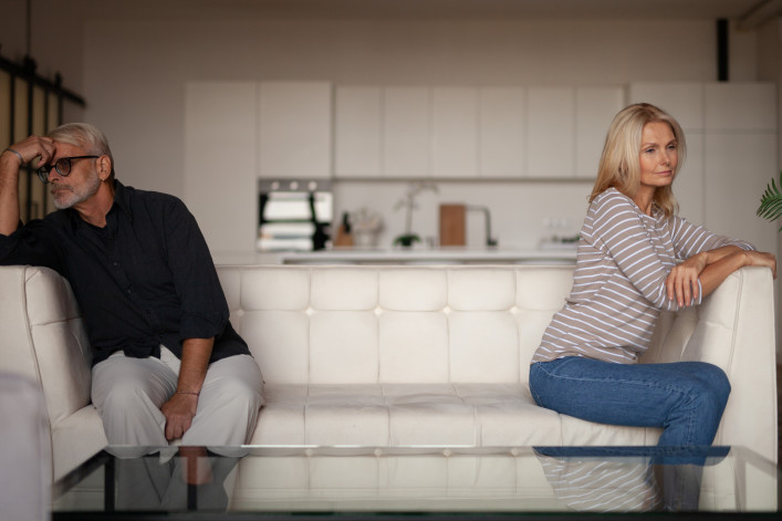 Quarrel in a mature family. Senior husband and wife are sitting on opposite sides of the sofa in the interior of the apartment. Relationship difficulties stock photo