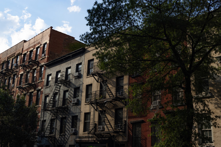 A row of colorful old brick apartment buildings and residential buildings with fire escapes along a street in Chelsea of New York City.