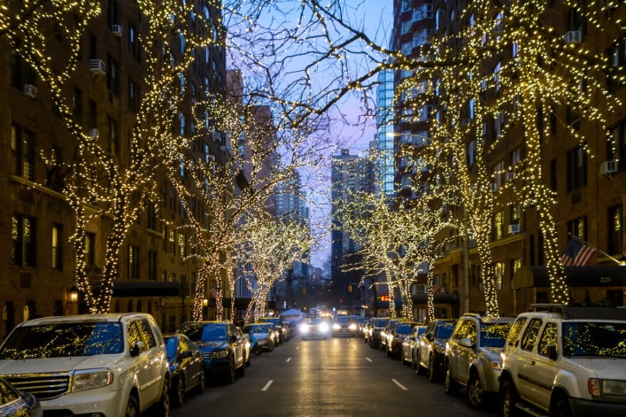 New york city street and brownstone buildings with trees covered in Christmas white lights one point perspective car dusk or early morning stock photo