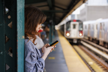 Woman checking her phone on an elevated subway platform