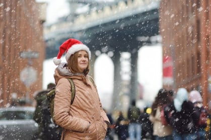 A young woman in a Santa Claus hat walks during a snowfall in NYC with Manhattan Bridge in the background