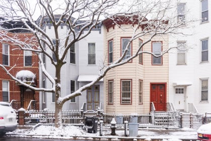 This is a front view of several residential buildings side by side along a street with snow on a winter day in Brooklyn, New York.