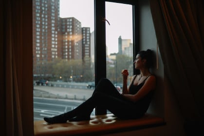 Young woman having an apple, relaxing by the window, enjoying the view in Manhattan, New York.