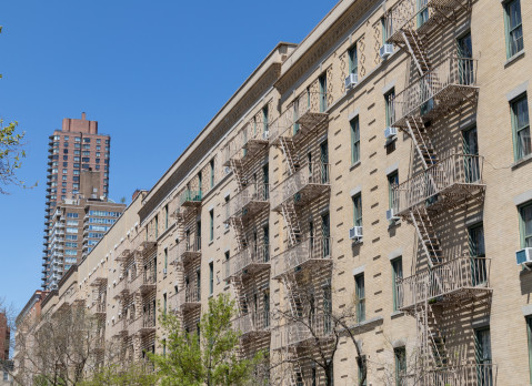 A row of similar old brick residential buildings with fire escapes on the Upper East Side of New York City