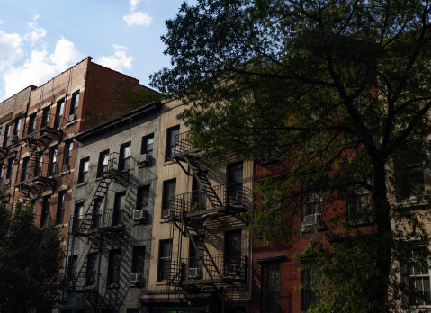 A row of colorful old brick apartment buildings and residential buildings with fire escapes along a street in Chelsea of New York City.