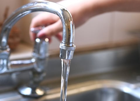 faucet with hand of woman in kitchen for cleaning, drinking and washing dishes. Interior, steel and household plumbing with sink and tap at home for stream, flowing and splash