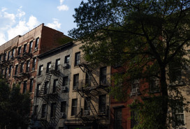 A row of colorful old brick apartment buildings and residential buildings with fire escapes along a street in Chelsea of New York City.