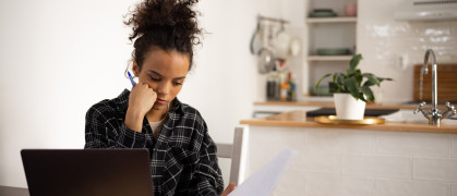 Young Black woman looking at documents at home, using a laptop