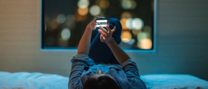 Woman lying down on bed and using smart phone at night stock photo