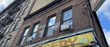New York, NY USA - December 6, 2023 : Hand-painted yellow and red "Sweet Corner Grocery Corp." sign over a deli on a two-story brick apartment building in Harlem, New York City