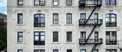 Front view of white pre-war apartment building facade seen from elevated subway station in Morningside Heights, Manhattan, New York City