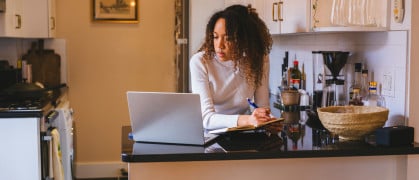 A young lady studying at the kitchen counter, utilizing a laptop and notepad.