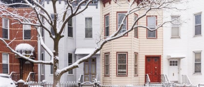 This is a front view of several residential buildings side by side along a street with snow on a winter day in Brooklyn, New York.